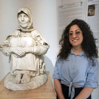 La guida turistica Maria Grazia Hussain Tedde accanto alla scultura "La Madre dell'ucciso" di Francesco Ciusa, unica versione marmorea firmata dall'artista, custodita presso il Museo delle Migrazioni, Cammini e Storie di Popoli di Pettinengo.